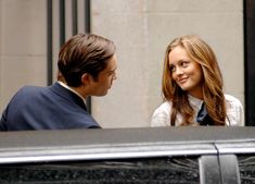 a man and a woman sitting next to each other in front of a black car