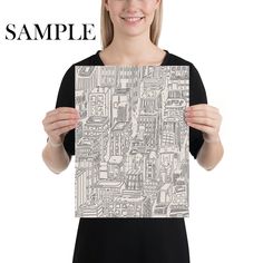 a woman holding up a piece of paper with buildings on it and the words sample