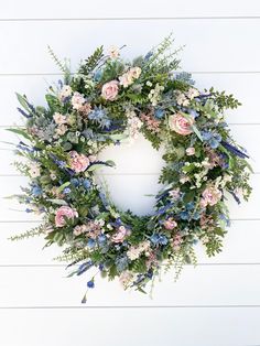 a wreath with flowers and greenery hanging on a white wooden wall in front of a door