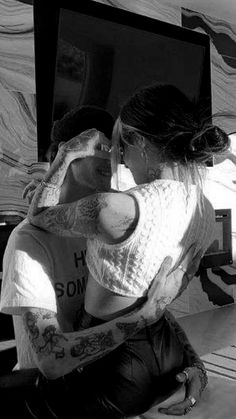 two people hugging each other in front of a computer screen with tattoos on their arms