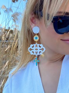 A unique pair of evil eye earrings that are made from plexiglass and metal parts in Gold, Turquoise and White colors with special pendant charms. They open and close with hypoallergenic clip on parts.  Find them only at  Christina Christi Store. DIMENSIONS - Total length of Long Earrings: 12 cm (4.72'') - Max Width 6 cm (0.98'') MATERIALS - Plexiglass Parts. - Metal Parts. - Clip On Earrings. PROTECTION - Protect them from water, perfumes, hair and body lotion to keep them bright and shiny for y White Spiritual Dangle Earrings, Spiritual White Dangle Earrings, White Spiritual Teardrop Earrings, Unique White Pierced Earrings, White Spiritual Pierced Jewelry, Handmade White Dangle Plug Earrings, White Earrings With Dangling Charms For Gift, Elegant Dangle Earrings With Evil Eye, White Bohemian Jewelry With Dangling Charms