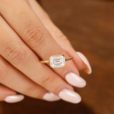 a woman's hand holding a ring with a diamond on it and white nails