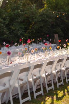 a long table set up with white chairs and flowers in vases on each side