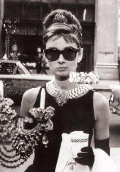 a woman walking down the street in sunglasses and a dress with pearls on it's neck