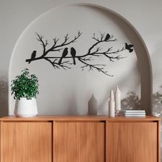 two birds sitting on a tree branch metal wall art in an arch above a wooden cabinet