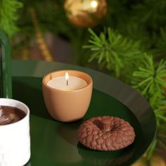 a cup of coffee and a cookie on a green tray next to a christmas tree