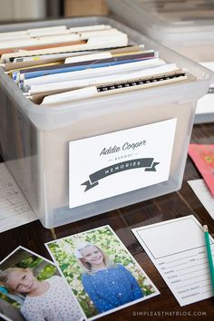 a plastic container filled with files and photos on top of a table next to papers