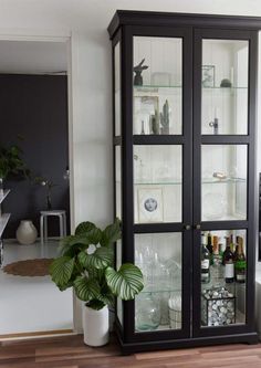 a tall black cabinet with glass doors and shelves filled with bottles, glasses, and other items