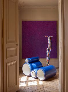 two rolls of blue paint sitting on top of a wooden floor next to a purple wall