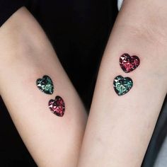 two heart shaped tattoos on both arms, one with green and red crystals in the shape of hearts