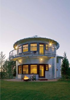 a round house with an outdoor fire pit in the middle of it at dusk, surrounded by trees and grass