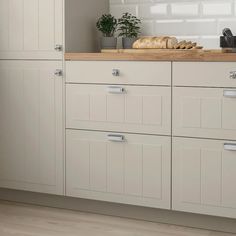 a kitchen with white cabinetry and wood flooring is pictured in this image, there are bread on the counter