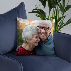 an elderly couple hugging each other on a blue couch in front of a plant and potted palm tree