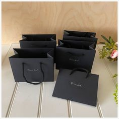 four black shopping bags sitting on top of a white table next to a vase with flowers