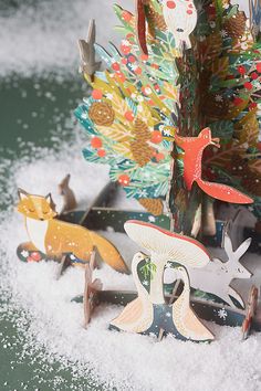 christmas decorations are sitting in the snow on top of a tree branch with birds and deer