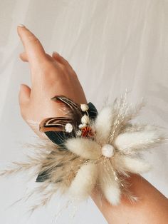 a person's hand with a wrist corsage made out of feathers and flowers