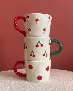 three ceramic cups are stacked on top of each other with cherries painted on them