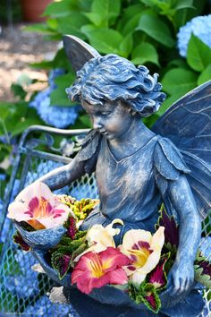 a statue of a fairy holding flowers on a bench in front of some blue hydrangeas