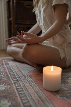 a woman sitting on the floor in front of a lit candle with her hands together