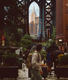 people are walking on the sidewalk under an overpass in new york city, with skyscrapers in the background