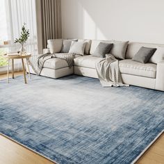 a living room with a large blue rug and white couch in the corner, on top of a hard wood floor