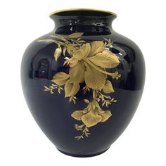 a black vase with gold flowers painted on the front and sides, against a white background