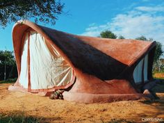 an unusual house made out of clay in the middle of a dirt field with trees around it