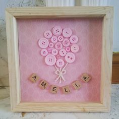 a wooden frame with some pink buttons in the shape of a heart and name spelled by scrabbles