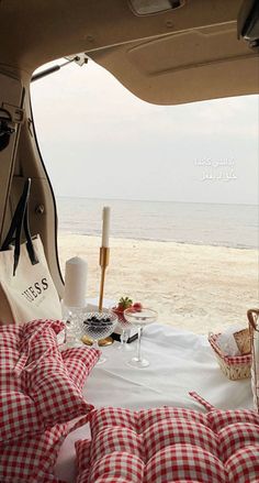 a table with food and drinks in the back of a vehicle on the beach next to the ocean