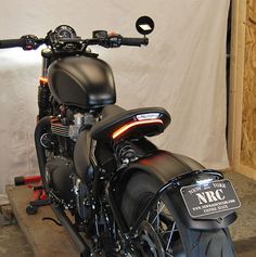 a black motorcycle parked in a garage next to a white wall and some wooden planks