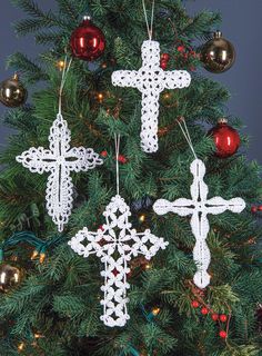 three crocheted crosses hanging from a christmas tree with baubles on it