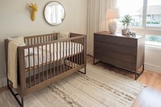 a baby crib in the corner of a room next to a dresser and window