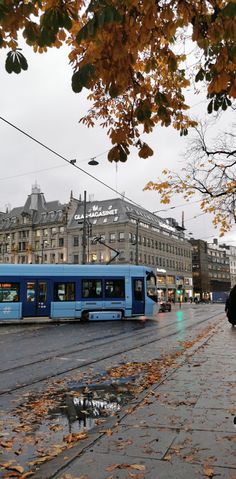 a blue train traveling down a street next to tall buildings on either side of it