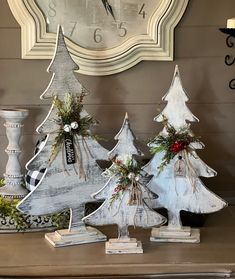 three wooden christmas trees sitting on top of a table next to a clock and potted plants