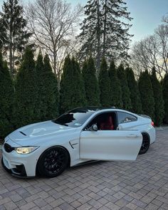 a white car parked on top of a brick road next to some trees and bushes