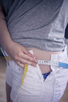 a person measuring their waist with a tape measure stick in front of her back pocket