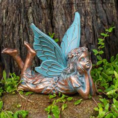 a statue of a fairy laying on its side next to a tree