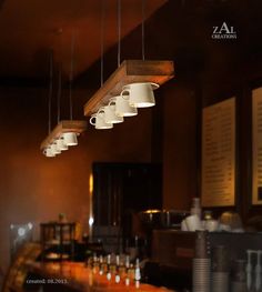 several lights hanging from the ceiling above a bar with cups on it's counter