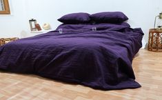 a bed with purple sheets and pillows on top of it in a room next to a wooden floor