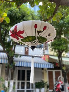 a paper lantern hanging from a tree in front of a building with flowers on it