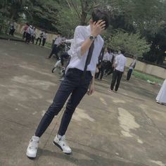 a young man in white shirt and tie holding his hand to his face while standing on concrete