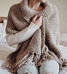 a woman sitting on top of a bed wearing a knitted shawl