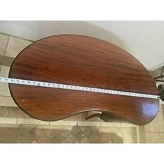 a wooden guitar sitting on top of a tile floor next to a measuring tape in front of it