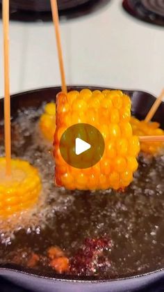 corn on the cob being cooked in a frying pan with chopsticks