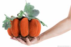 a hand holding a small stuffed pumpkin with leaves on it's top and two smaller ones in the middle