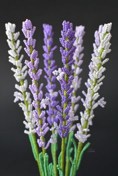 purple and white flowers are in a vase on a table with green stems, against a black background