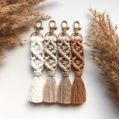 four tasselled keychains sitting on top of a white surface next to dried grass