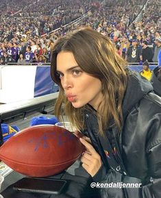 a woman holding a football in front of a crowd at a game with her tongue out