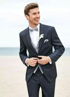 a man in a tuxedo smiles as he adjusts his bow tie on the beach