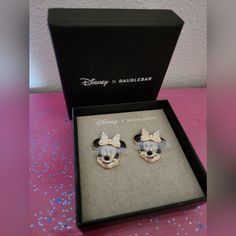 two mickey mouse earrings in a box on a pink table with blue and white confetti